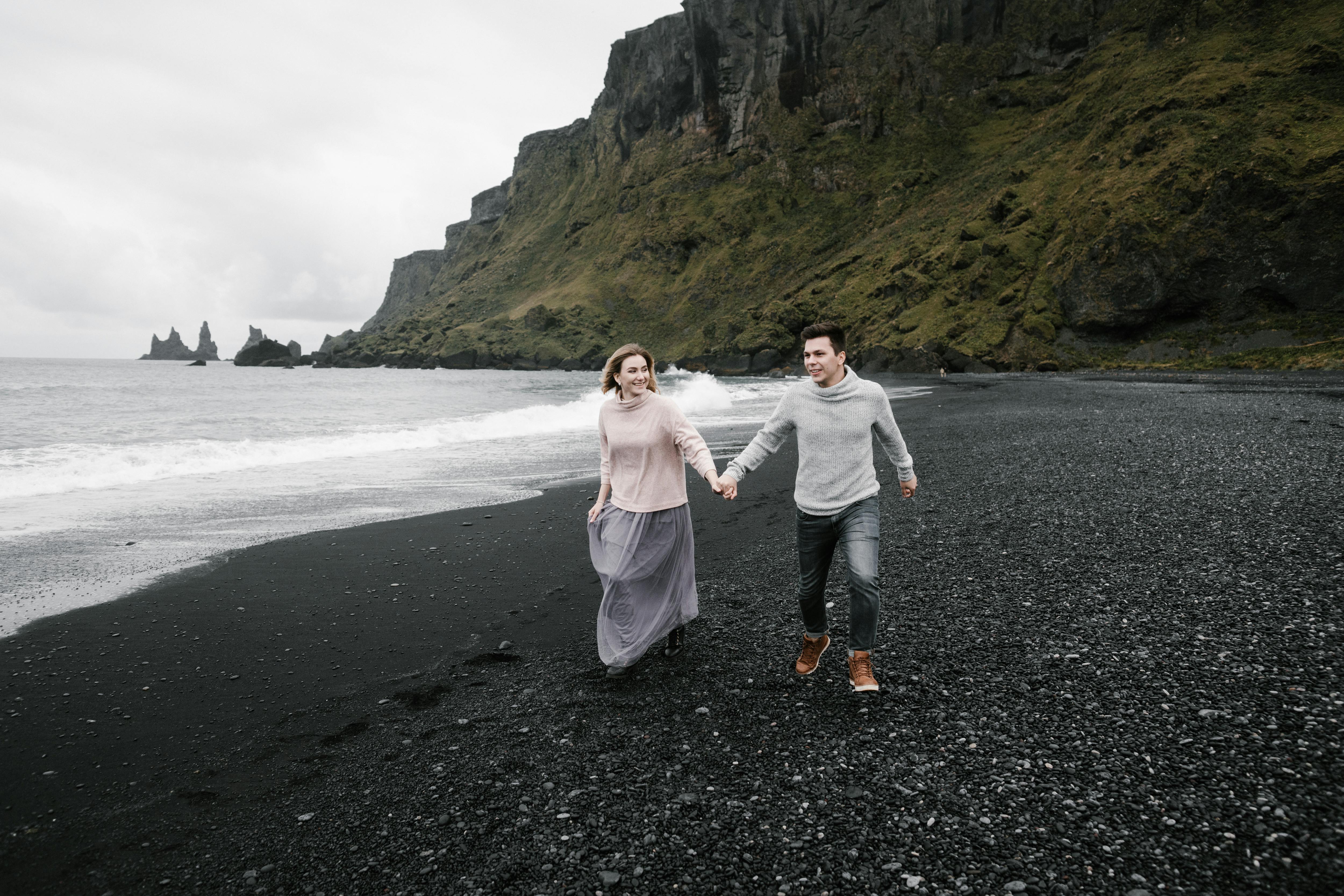 couple marchant sur une plage de sable noir en Islande